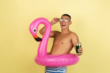 Sarı stüdyo arka planında izole edilmiş yüzme şortlu yakışıklı Asyalı adamın portresi..