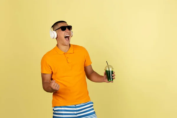 One young smiling handsome asian man in bright summer clothes with headphones isolated over yellow studio background. — 스톡 사진