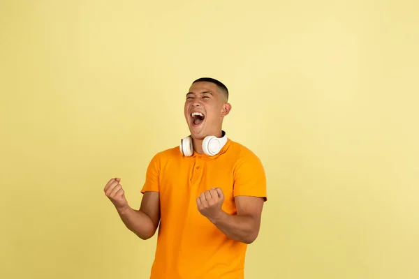Um jovem sorrindo bonito asiático homem em roupas de verão brilhante com fones de ouvido isolados sobre amarelo estúdio fundo. — Fotografia de Stock