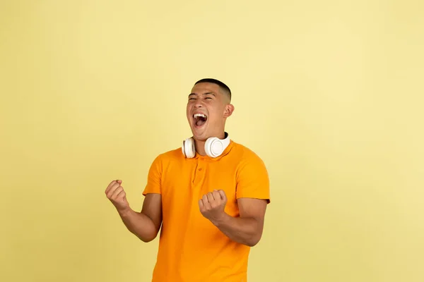 Ein junger lächelnder gutaussehender asiatischer Mann in heller Sommerkleidung mit Kopfhörern auf gelbem Studiohintergrund. — Stockfoto