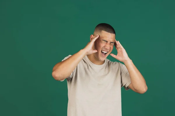 Retrato de jovem bonito asiático homem em t-shirt tendo dor de cabeça isolado sobre escuro verde estúdio fundo. — Fotografia de Stock