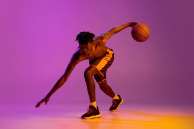 Genç Afrikalı, basketbol oyuncusu, topla hareket eden, mor neon arka planda izole edilmiş..