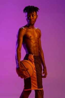 Genç Afrikalı bir adam, topuyla duran basketbolcu mor neon arka planda izole edilmiş..