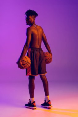 Genç Afrikalı bir adam, basketbol oyuncusu iki topla poz veriyor. Mor neon arka planda izole edilmiş. Arka plan