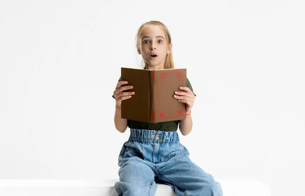 Портрет девочки-кавказки в повседневной одежде, читающей книгу на белом фоне студии. — стоковое фото