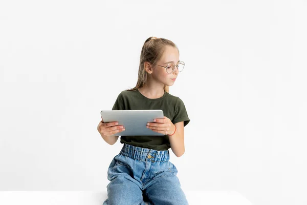 Jeden chytrý teen škola běloška dívka v ležérní oblečení a brýle drží tablet izolované přes bílé studio pozadí. — Stock fotografie