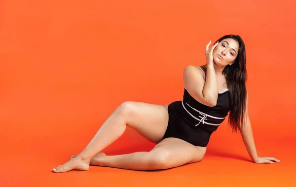 Young beautiful plump woman in black underwear on orange background — Stock Photo, Image