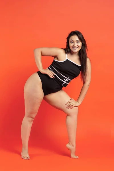 Young beautiful plump woman in black underwear on orange background