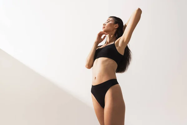Studio image of young beautiful woman with slim figure in black underwear posing over white studio background — Stock Photo, Image