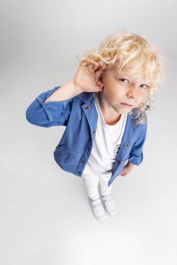 Beyaz stüdyo arka planında izole edilmiş kameraya bakan günlük kıyafetli, tatlı, kıvırcık bir anaokulu çocuğu..