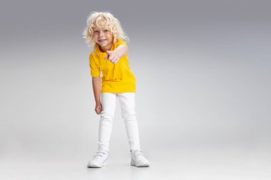 Küçük tatlı kıvırcık okul çocuğu eğleniyor, beyaz stüdyo arka planında soyutlanmış oynuyor..