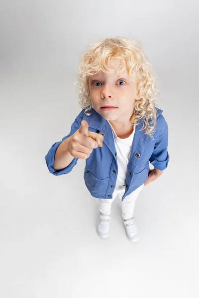 흰색 스튜디오 배경 위에 격리되어 있는 카메라 를 보고 있는, 평상복을 입은 작고 곱슬곱슬 한 미취학 아동. — 스톡 사진