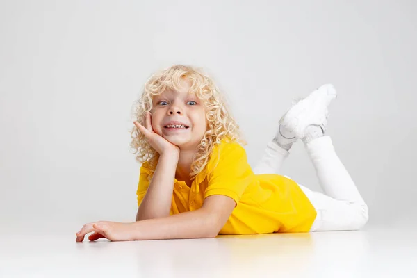 Söt liten lockigt förskola pojke att ha kul, spela isolerad över ljus studio bakgrund. — Stockfoto