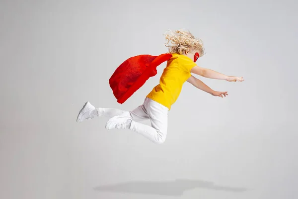 Schattig klein krullend voorschoolse jongen in rode cape en masker vliegen geïsoleerd over witte studio achtergrond. — Stockfoto