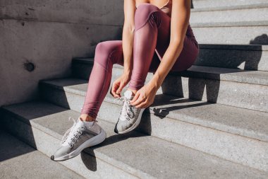 Spor kıyafetleri içinde genç, zayıf, sportif beyaz kadın şehir sokaklarındaki eğitimden sonra merdivenlerde dinleniyor.