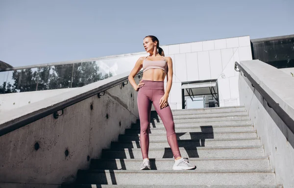 Νεαρή λεπτή αθλητική καυκάσια γυναίκα γυμνάζεται, κάνει γυμναστική, γιόγκα στις σκάλες σε εξωτερικούς χώρους. — Φωτογραφία Αρχείου