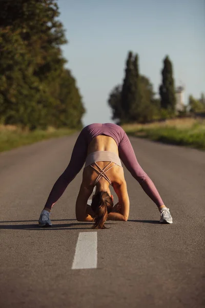 One young slim sportive caucasian woman working out, doing fitness on the open road. — Stock Photo, Image