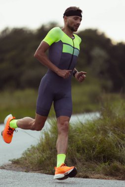 Genç profesyonel erkek triatloncunun tam boy görüntüsü, açık yolda koşan bir koşucu. Spor anlayışı, yaşam tarzı, aktivite.