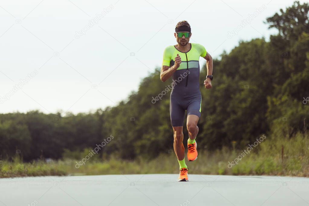 Young professional male triathlete, runner in motion on open road. Concept of sport, lifestyle, activity