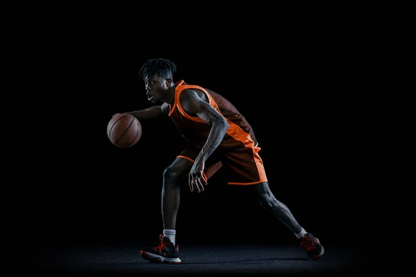 Studio immagine di giovane uomo africano, giocatore di basket praticare con la palla isolata su sfondo scuro studio. — Foto Stock