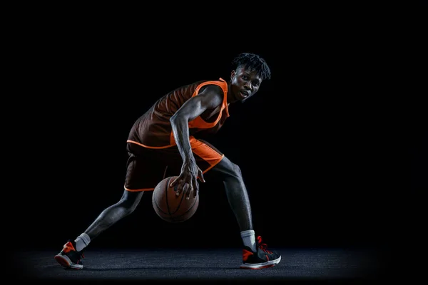한 젊은 아프리카 남자, 어두운 녹음실 배경 위에서 고립된 채 공을 가지고 연습하고 있는 농구 선수. — 스톡 사진