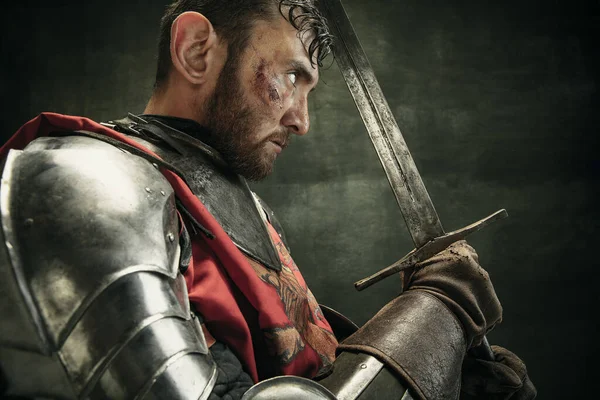 Vista lateral. Retrato de un hombre barbudo brutal, guerrero medeival o caballero con sucia cara herida sosteniendo espada — Foto de Stock