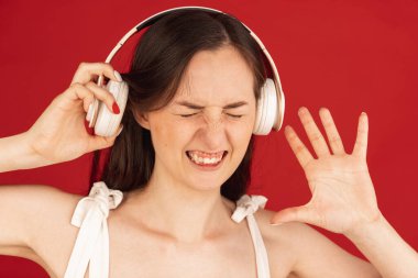 Parlak kırmızı arka planda izole edilmiş kulaklıklı sıradan bir beyaz kadın..