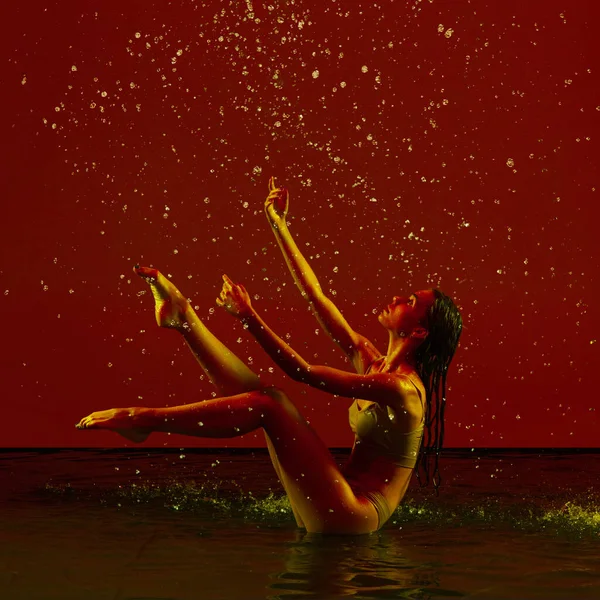 Piękno i wdzięk. Jedna młoda piękna balerina tańcząca w deszczu nad czerwonym tłem w neonowym świetle. — Zdjęcie stockowe