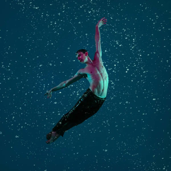 Jeden młody baletnica mężczyzna w ruchu, akcja w deszczu nad niebieskim tle w świetle neonu. — Zdjęcie stockowe