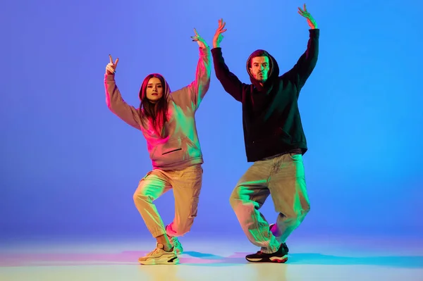 Deux jeunes gens, homme et femme dansant freinant, hip-hop sur fond bleu au néon. — Photo