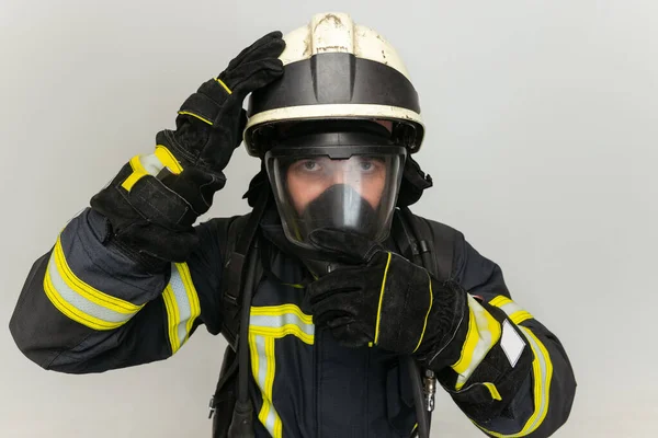 Seorang petugas pemadam kebakaran berpakaian seragam berpose di atas latar belakang studio putih. — Stok Foto