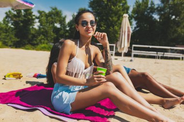 Mayolu genç kadınlar plajda dinleniyor, soğuk içecekler içiyor, eğleniyor, güneşleniyor.