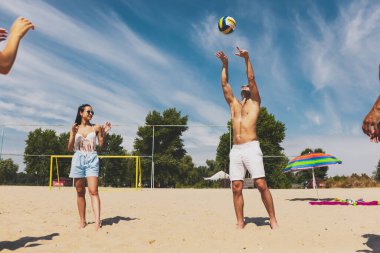 Bir grup genç, erkek ve kadın plajda dinleniyor, soğuk içecekler içiyor, eğleniyor, güneşleniyor.