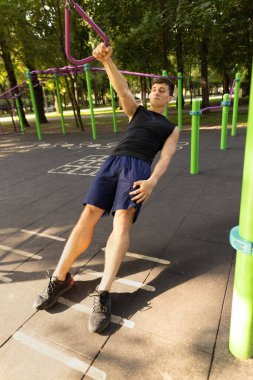 Spor kıyafetli yakışıklı beyaz bir adam parlak bir yaz gününde spor sahasında yaya geçidinde koşuyor..