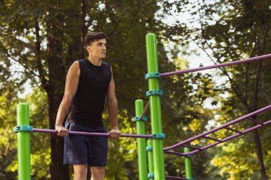 Spor kıyafetli yakışıklı beyaz bir adam parlak bir yaz gününde spor sahasında yaya geçidinde koşuyor..