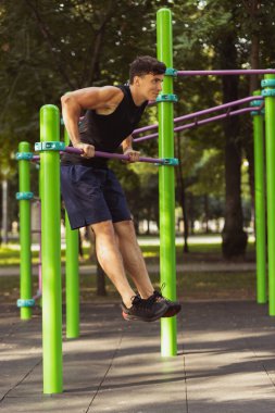 Spor kıyafetli yakışıklı beyaz bir adam parlak bir yaz gününde spor sahasında yaya geçidinde koşuyor..