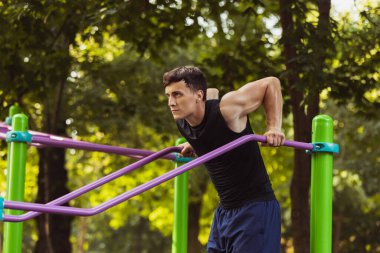 Spor kıyafetli yakışıklı beyaz bir adam parlak bir yaz gününde spor sahasında yaya geçidinde koşuyor..