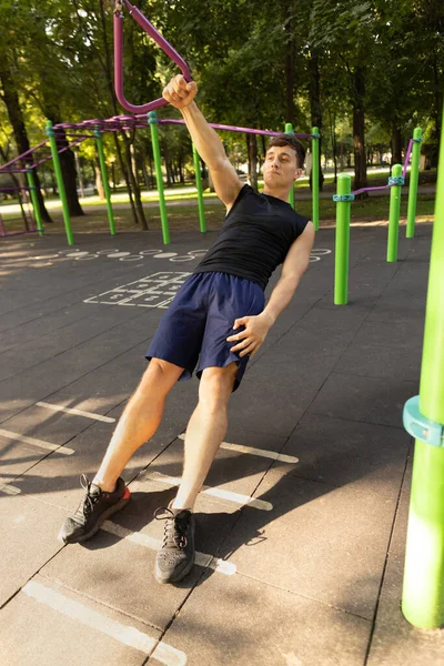 En ung stilig kaukasiska man i sportkläder gör crossfit på idrottsplats på ljusa sommardag. — Stockfoto