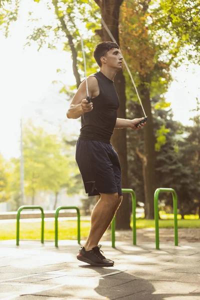 stock image One young handsome caucasian man in sportswear jumping with rope at crossfit ground on bright summer day.