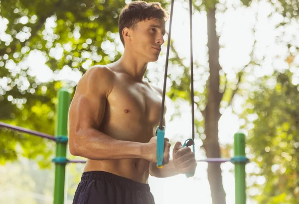 Un joven guapo hombre caucásico haciendo ejercicios para bíceps y tríceps en el suelo crossfit en el día de verano brillante. — Foto de Stock