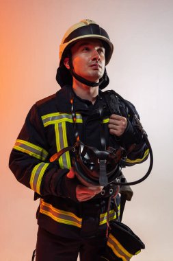 Yakın plan. Üniformalı bir erkek itfaiyeci turuncu arka plan üzerinde neon ışıklarla poz veriyor..