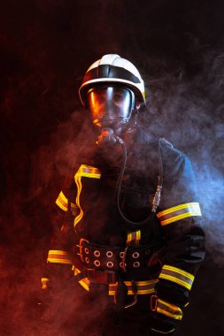 Siyah arka plana karşı poz veren üniformalı bir itfaiyeci dumanla kaplı.