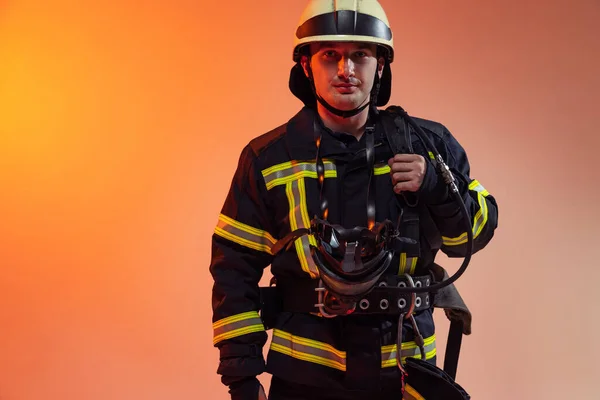 一名身穿制服的男性消防员在霓虹灯下摆出橙色背景的姿势. — 图库照片