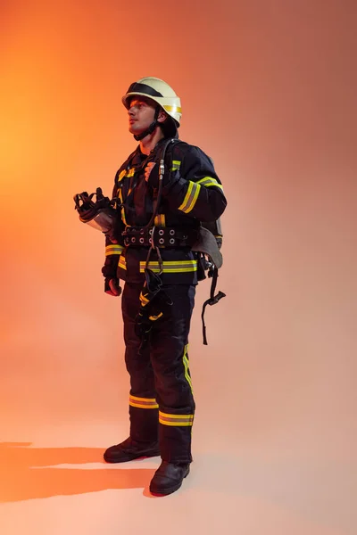 Un bombero masculino vestido de uniforme posando sobre fondo naranja con luces de neón. —  Fotos de Stock