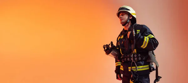 Volador. Un bombero masculino vestido de uniforme posando sobre fondo naranja con luces de neón. —  Fotos de Stock