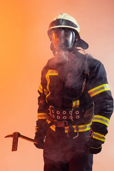 一名身穿制服的消防员在烟雾弥漫的橙色背景下摆姿势 — 图库照片