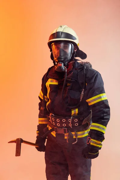 Üniformalı bir itfaiyeci, dumanla kaplı turuncu bir arka planda poz veriyor. — Stok fotoğraf