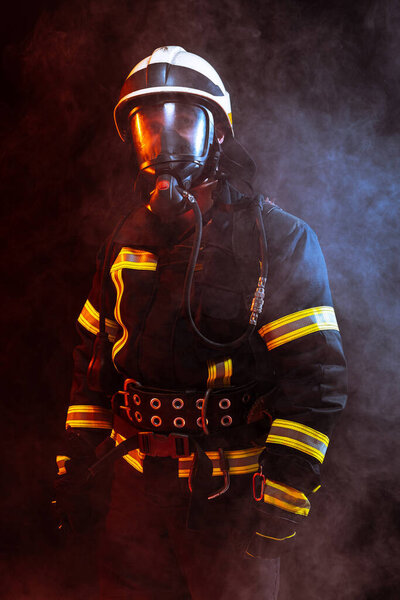 One uniformed firefighter posing against black background covered in smoke