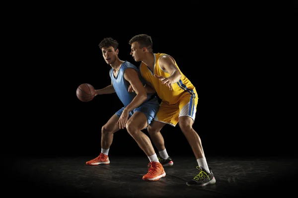 Competitive sport. Two male athletes, professional basketball players in action, motion isolated over black background.