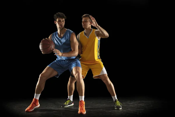 Konkurrenskraftig sport. Två manliga idrottare, professionella basketspelare i aktion, rörelse isolerad över svart bakgrund. — Stockfoto